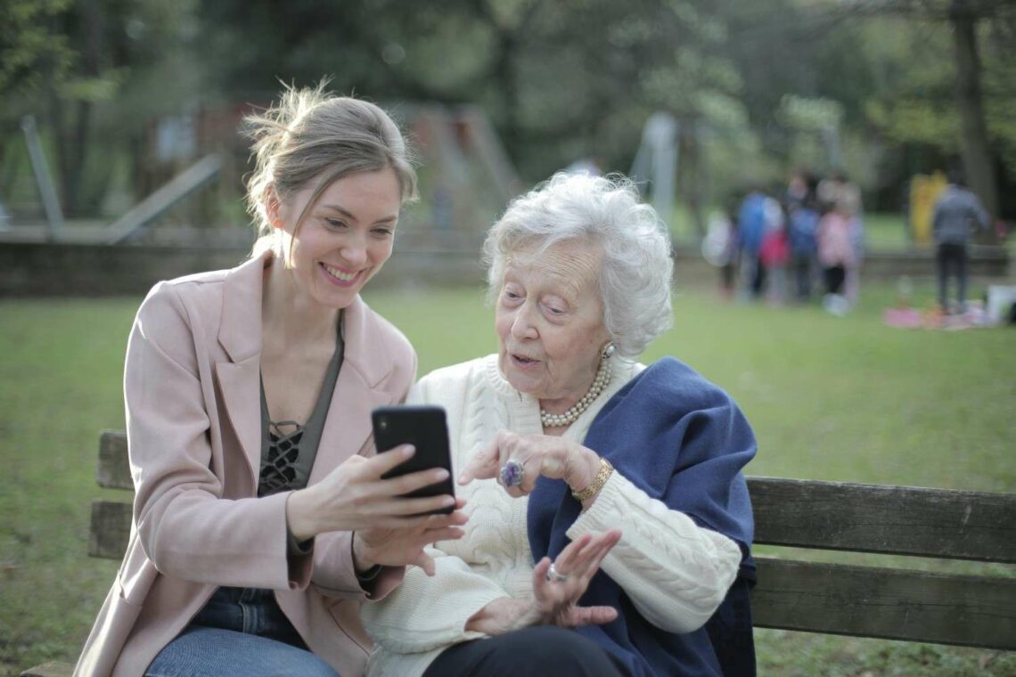Young woman helping an elderly woman use a smartphone while sitting on a park bench