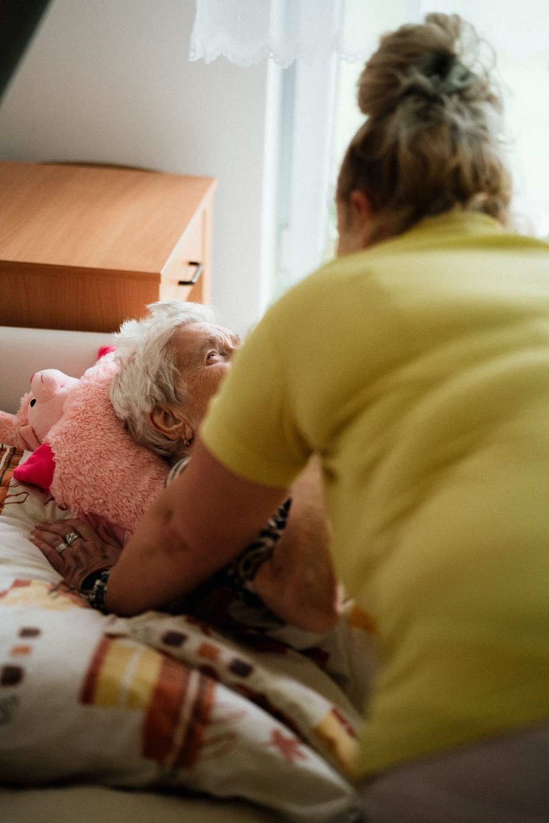 A caregiver assists an elderly woman in bed, providing support and comfort during her time of need.