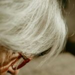 A senior woman with glasses and white hair, looking thoughtfully while sitting in a well-lit room.