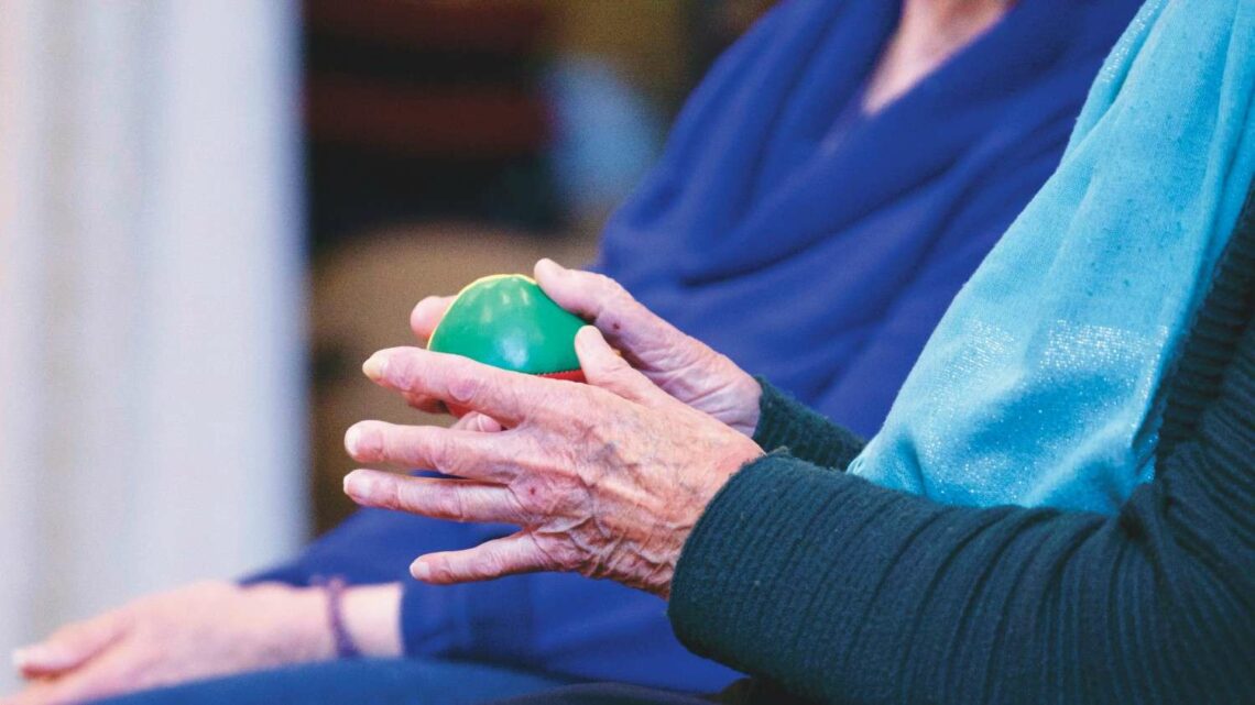 Older adult exercising arthritic hands with a soft stress ball during physiotherapy.