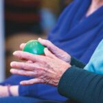 Older adult exercising arthritic hands with a soft stress ball during physiotherapy.