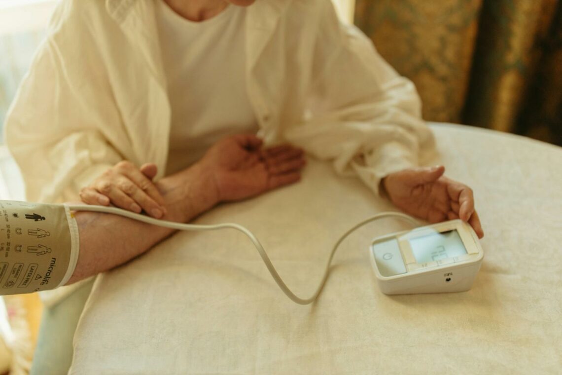 Older adult checking blood pressure at home using an electronic monitor.