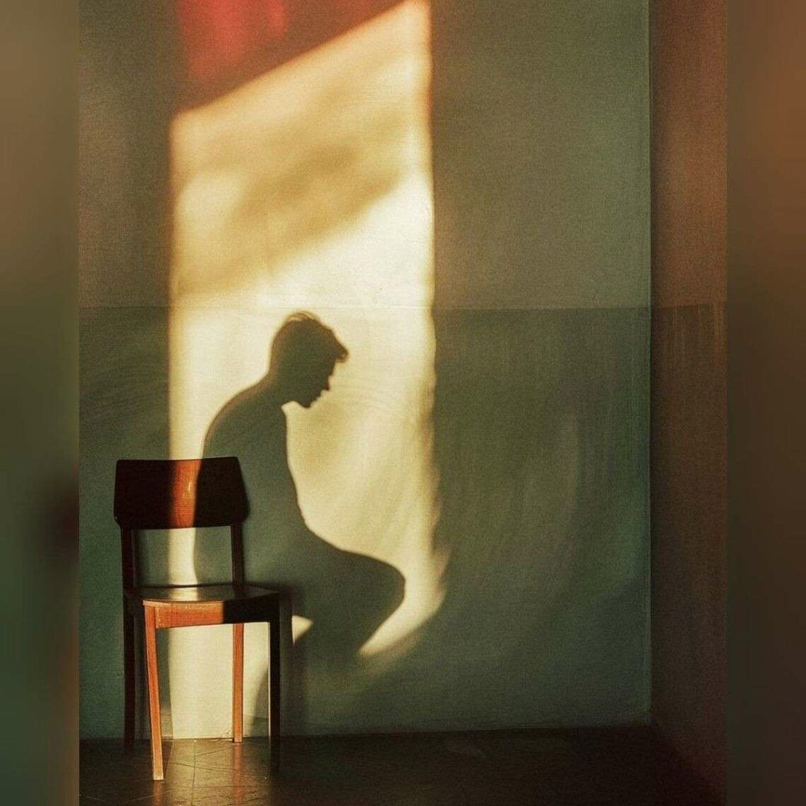 A man sitting on a chair, gazing out of a window, with natural light illuminating the room.