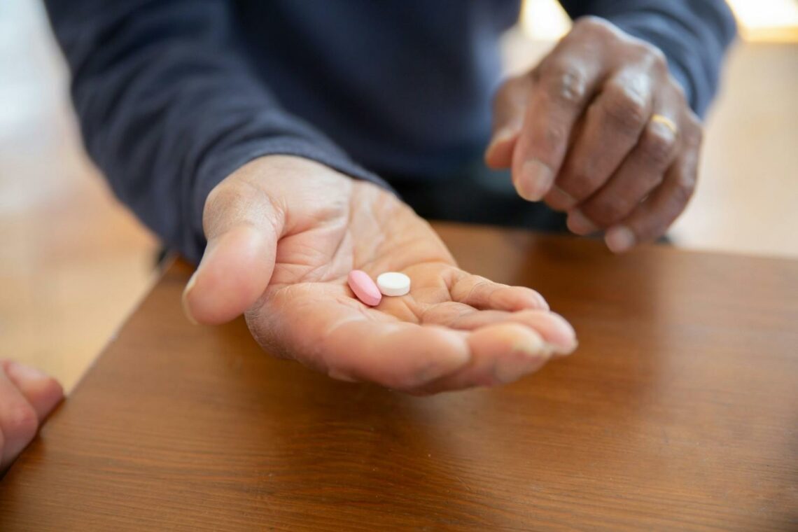 A person holding two tablets in the palm of their hand while pointing to them, sitting at a wooden table.