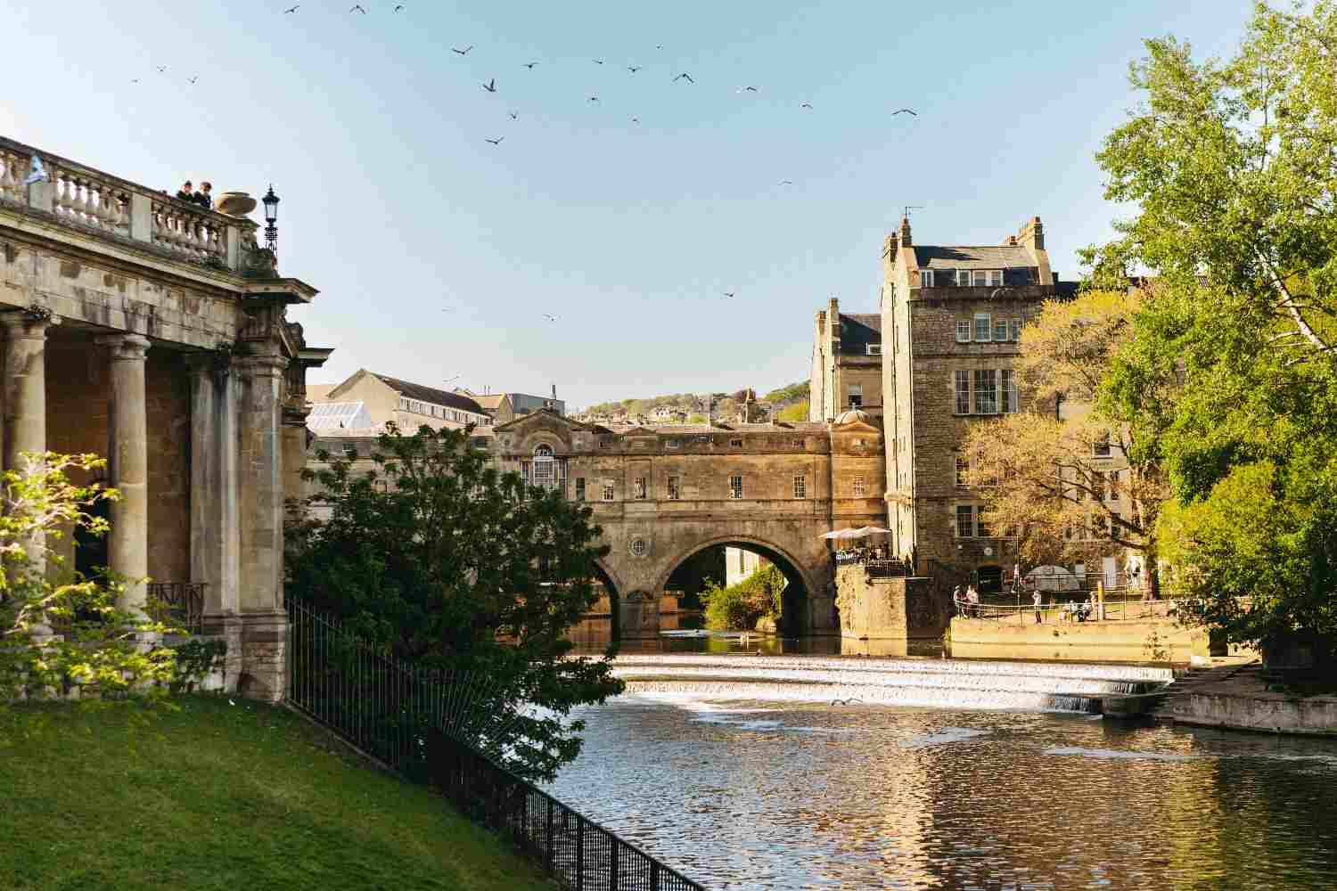 A scenic river with a bridge crossing over it, featuring a building in the background against a clear sky.