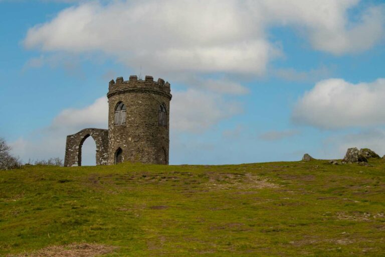 Stone tower and archway of Old John Tower on Bradgate Park hilltop in Leicestershire, under a blue sky with scattered clouds.