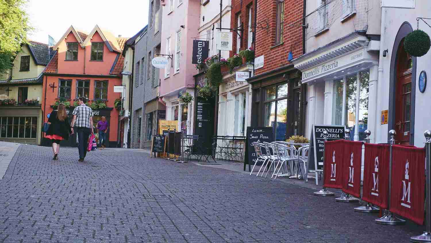 A brick-paved street bustling with pedestrians walking in various directions.