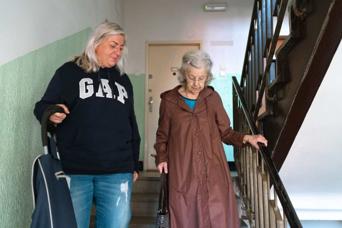 An older woman and a younger woman walking together down a stairway, sharing a moment of connection and support.