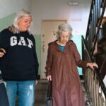 An older woman and a younger woman walking together down a stairway, sharing a moment of connection and support.