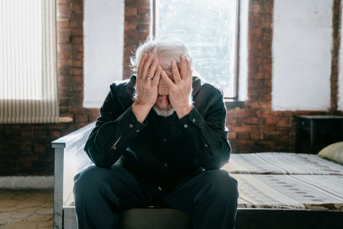 Elderly man with dementia aggression sitting with his head in his hands, showing signs of distress.