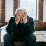 Elderly man with dementia aggression sitting with his head in his hands, showing signs of distress.