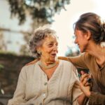 "Elderly woman sitting outdoors holding hands with a carer
