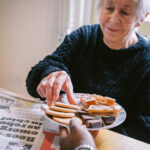 Carer offering biscuits to an elderly woman, showing comfort and companionship during mealtime.