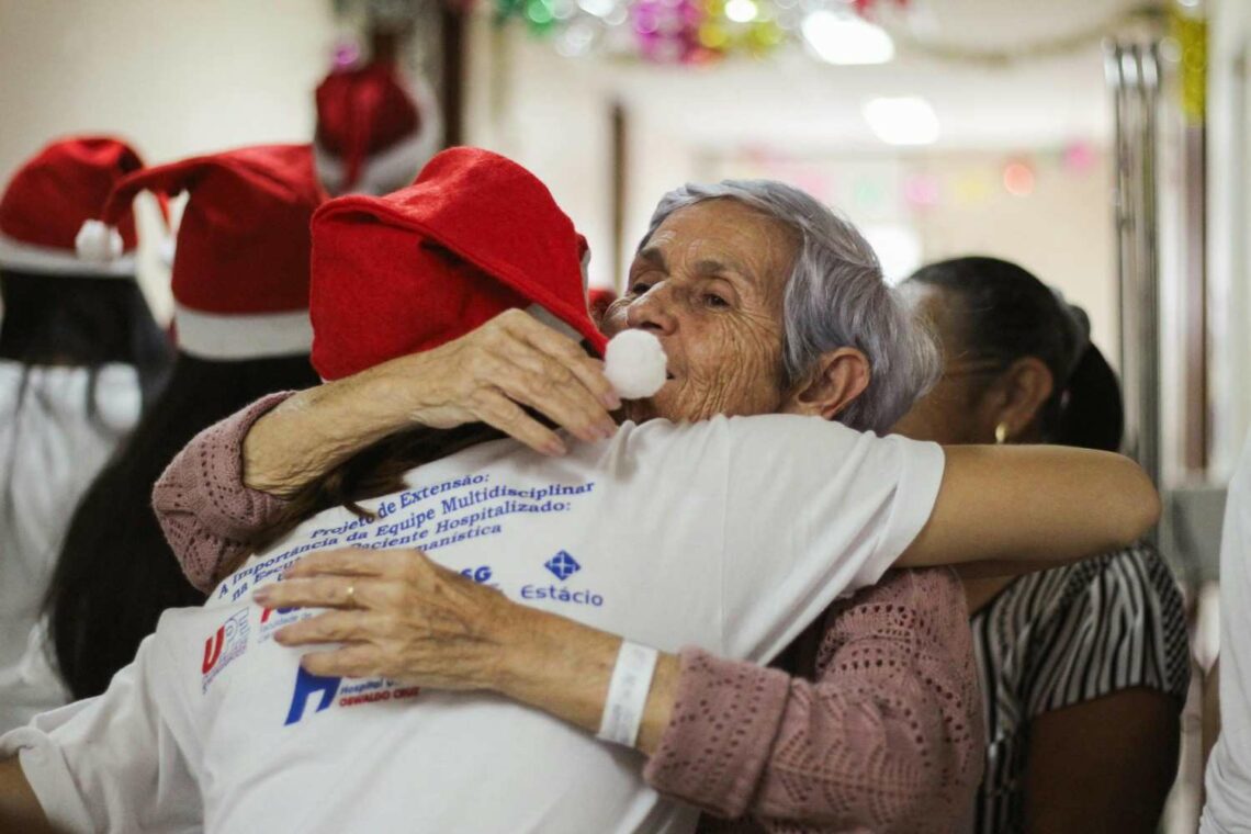 An older woman embraces someone wearing a Santa hat during a festive gathering, highlighting warmth, connection and holiday companionship.