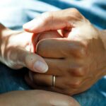 Close-up of two people holding hands gently, one wearing a simple ring, conveying comfort and support