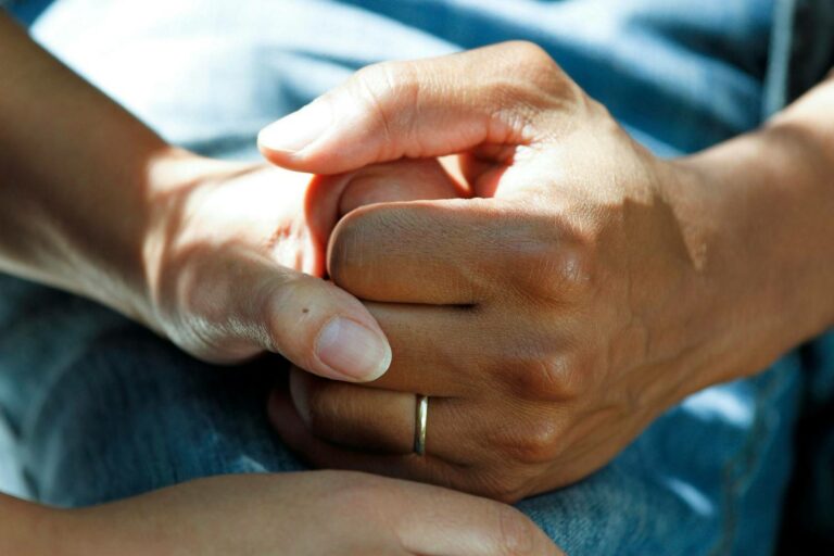 Close-up of two people holding hands gently, one wearing a simple ring, conveying comfort and support