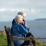 Elderly man and woman sitting together on a wooden bench overlooking the sea