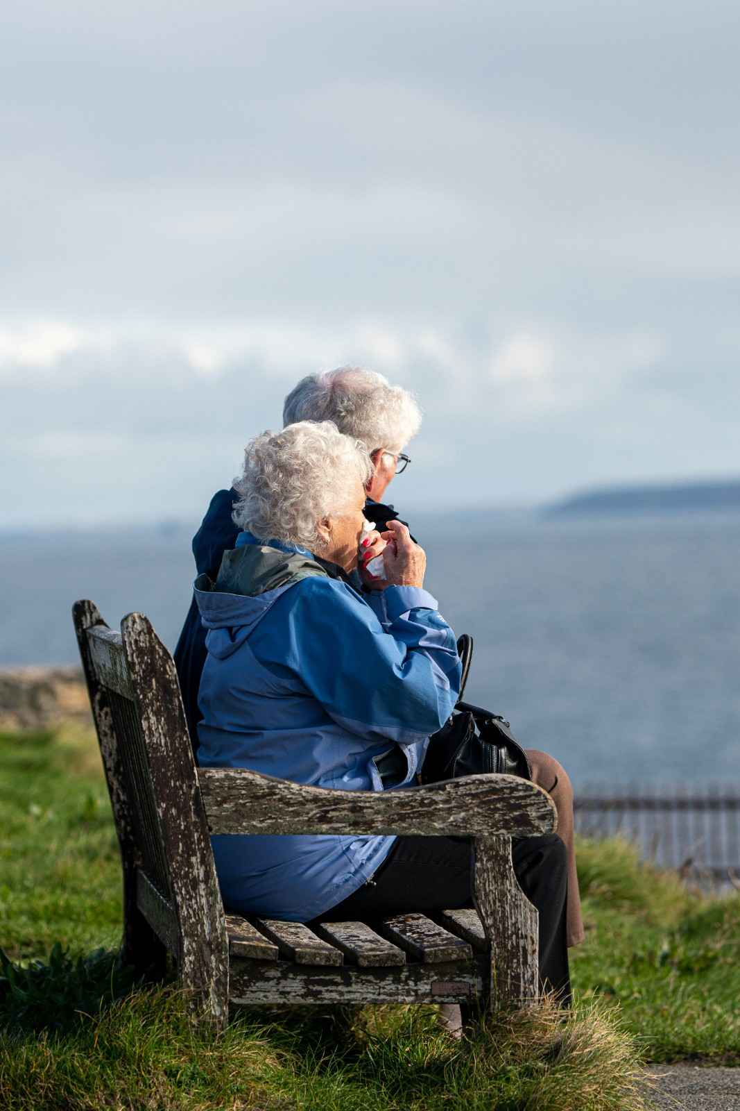 Elderly man and woman sitting together on a wooden bench overlooking the sea