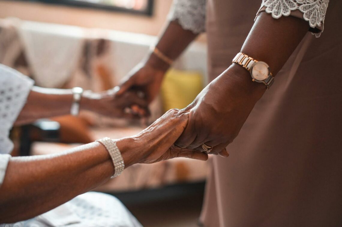 An older person and a younger person holding hands, with a bracelet and watch visible on each wrist