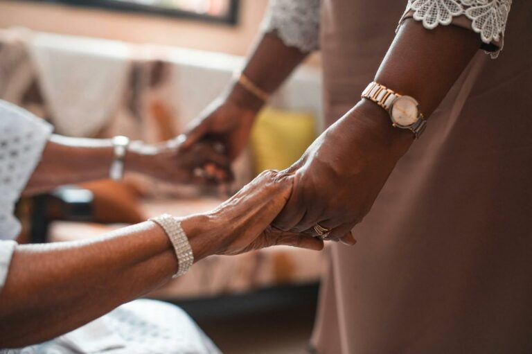 An older person and a younger person holding hands, with a bracelet and watch visible on each wrist