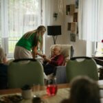 A woman assists an elderly woman in a cozy living room, providing support and companionship.