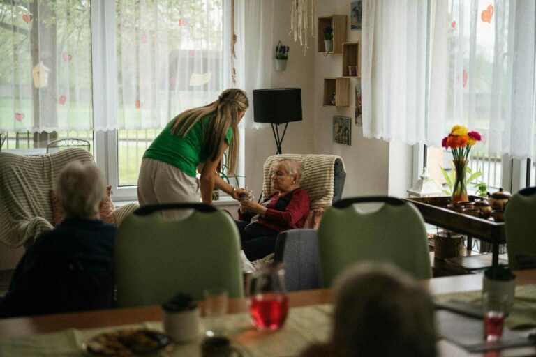 A woman assists an elderly woman in a cozy living room, providing support and companionship.
