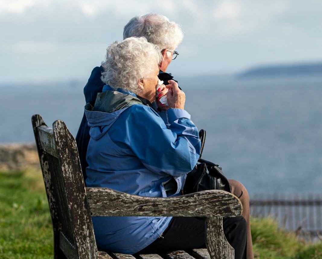 Two elderly individuals sitting together on a park bench, enjoying a peaceful moment outdoors.
