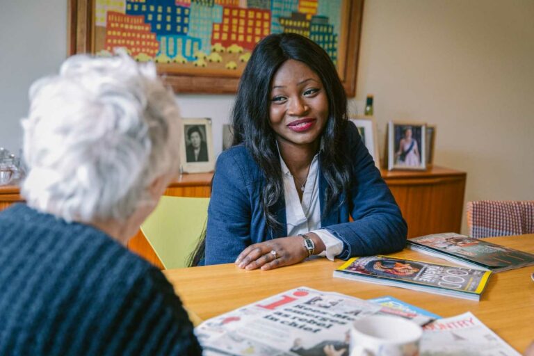 A woman and an older woman sit together at a table, engaged in conversation and sharing a warm moment.