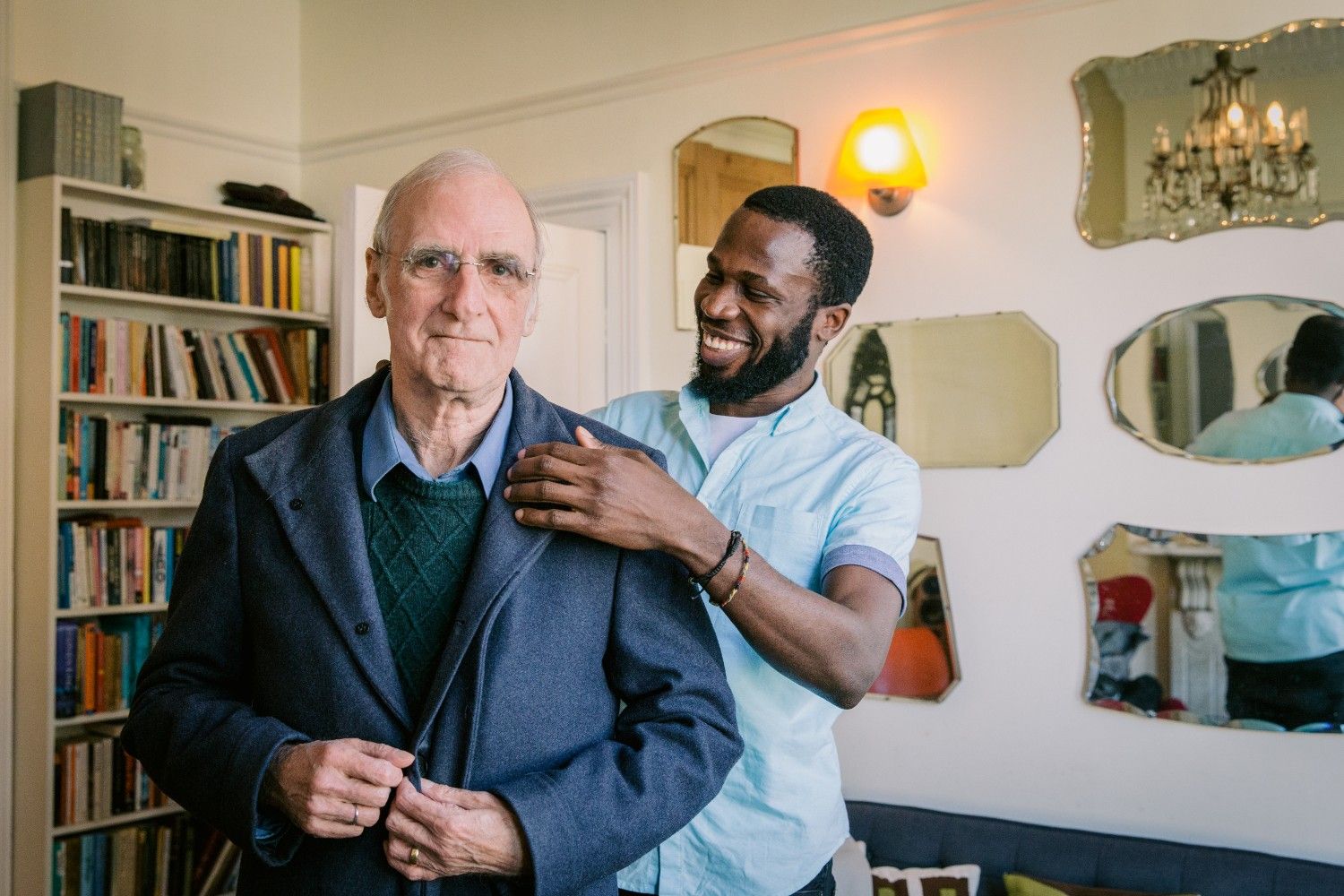 A younger man helps an older man, illustrating a moment of care and support between two individuals.