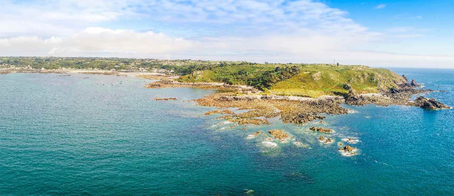 Aerial view of a coastline meeting the ocean, showcasing sandy beaches and gentle waves under a clear blue sky.