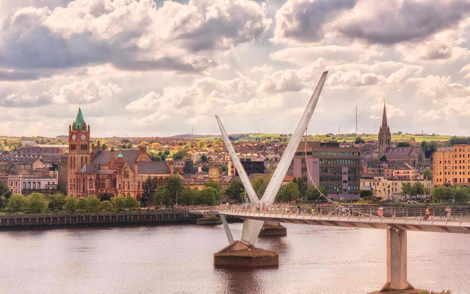 A bridge crosses a river, with a city skyline visible in the background under a clear blue sky.