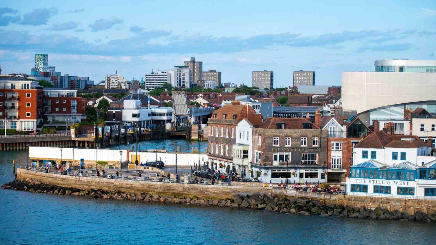 A vibrant city skyline in Hampshire with modern buildings alongside a bustling harbour filled with boats.